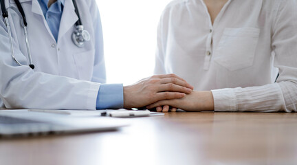 Doctor and patient sitting near each other at the wooden table in clinic. Female physician's hands...