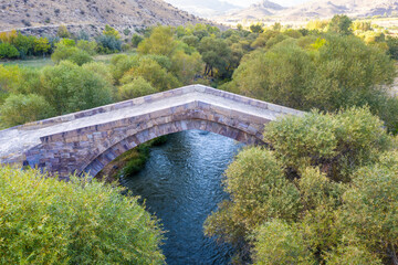 Drone view of old Dadal bridge over Arpa river on autumn evening. Yeghegnadzor, Vayots Dzor Province, Armenia.