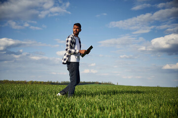 Standing and holding notepad. Handsome Indian man is on the agricultural field