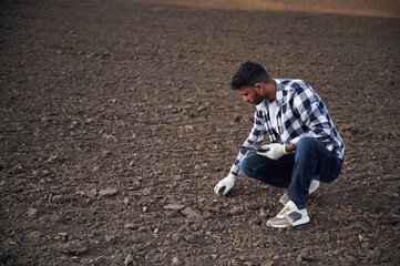 Cultivated agricultural field. Sitting, holding digital tablet. Handsome Indian man