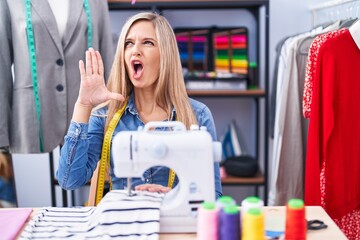 Blonde woman dressmaker designer using sew machine shouting and screaming loud to side with hand on mouth. communication concept.