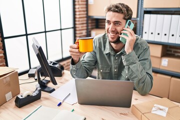 Young man ecommerce business worker talking on smartphone drinking coffee at office