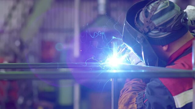 Welding work close-up. Welder worker weld pipe in protective helmet. Sparks fly out. Welding shop at Construction of Oil, Natural Gas and Fuels Transport Pipeline. Industrial Manufacturing Factory