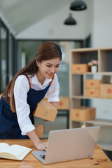 Starting small business entrepreneur of independent Asian woman smiling using computer laptop with cheerful success of online marketing package box items and SME delivery concept