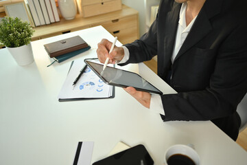 Cropped shot of businessman in black suit sitting at desk and using digital tablet. Business, technology and communication