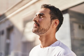 Young hispanic man looking to the sky with relaxed expression at street