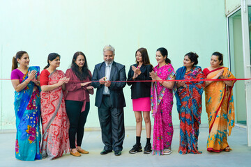 Naklejka premium Senior businessman cutting red ribbon with women employee group. inauguration concept.