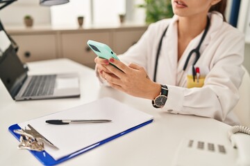 Young caucasian woman doctor using smartphone working at clinic