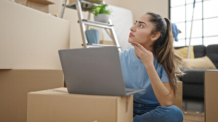 Young beautiful hispanic woman using laptop with doubt expression at new home