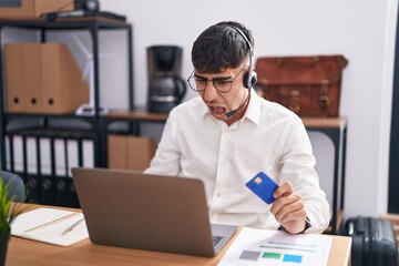 Young hispanic man working using computer laptop holding credit card angry and mad screaming frustrated and furious, shouting with anger. rage and aggressive concept.