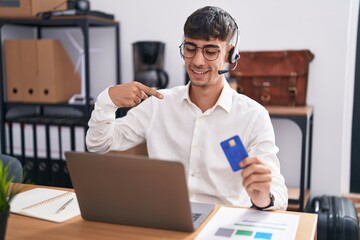 Young hispanic man working using computer laptop holding credit card looking confident with smile on face, pointing oneself with fingers proud and happy.