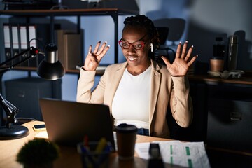 Beautiful black woman working at the office at night showing and pointing up with fingers number nine while smiling confident and happy.