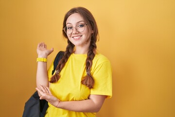 Young caucasian woman wearing student backpack over yellow background inviting to enter smiling natural with open hand