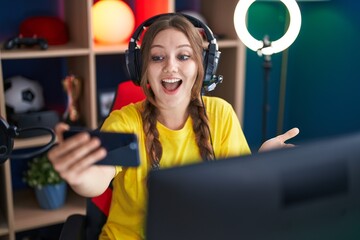 Young caucasian woman playing video games with smartphone celebrating achievement with happy smile and winner expression with raised hand