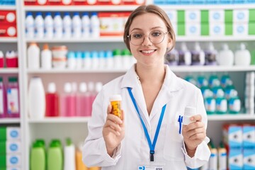 Young blonde woman pharmacist smiling confident holding two pills bottles at pharmacy