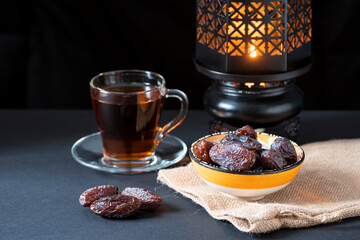 Dates, an oriental bowl with dates, a transparent cup with tea, a traditional lantern on a dark background