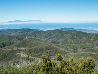 Fototapeta na wymiar View on La Palma island over laurel tree forest and hills of Garajonay National Park seen from peak of Alto de at Garajonay mountain. White clouds and blue sky above. La Gomera, Canary Islands, Spain.