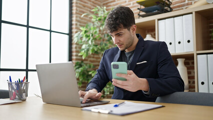 Fototapeta na wymiar Young hispanic man business worker using laptop and smartphone at office