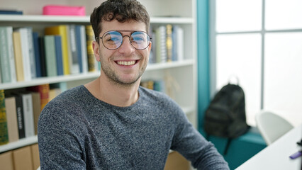 Young hispanic man student looking at the camera at library university