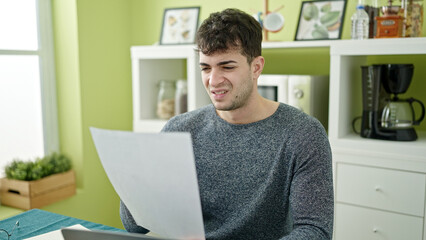 Young hispanic man reading document sitting on the table at dinning room