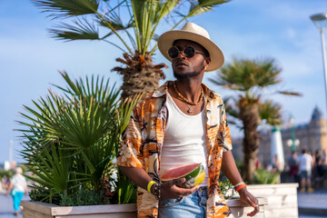 Black ethnic man enjoy summer vacation on the beach, sombrero and a watermelon