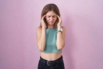 Blonde caucasian woman standing over pink background with hand on head, headache because stress. suffering migraine.