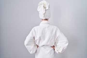 Blonde caucasian woman wearing bathrobe standing backwards looking away with arms on body