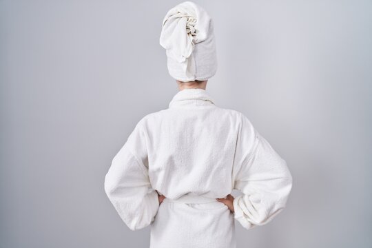 Blonde caucasian woman wearing bathrobe standing backwards looking away with arms on body