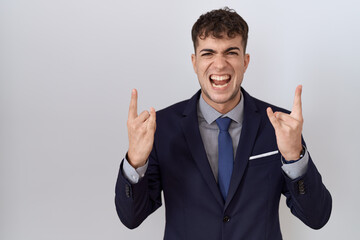 Young hispanic business man wearing suit and tie shouting with crazy expression doing rock symbol with hands up. music star. heavy concept.