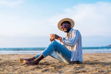 Portrait of a black ethnic man enjoy summer vacation at the beach eating a watermelon, Sitting on the sand