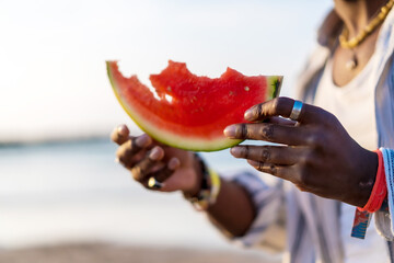 Hands of a black ethnic man enjoy the summer vacation on the beach eating a watermelon