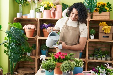 Young latin man florist watering plant at flower shop