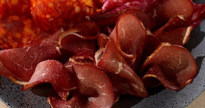 meat slices on a plate. traditional spanish sausage with beef jerky. salchichon, chorizo and prosciutto with glass of wine. serving cold cuts with dried tomatoes and bread. antipasto in sunlight.