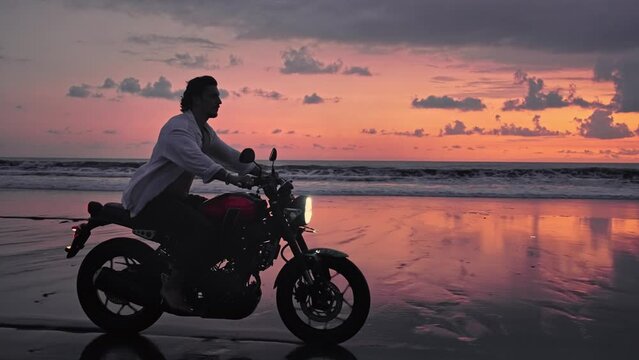 Motorbiker Riding Motorcycle or Traveling in Beautiful Nature of Beach Outdoors. Handsome Racer Man on Moto Bike with Power Motor Rides Sand in Fast Action. Freedom of Adult Person at Motorbike Trip