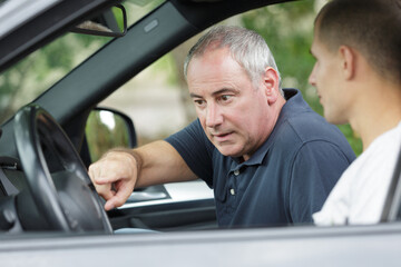 mature man explaining car controls to teenager