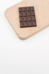 immagine primo piano di tavoletta di cioccolata fondente su tagliere in legno, sfondo bianco, vista dall'alto