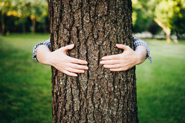 Unrecognizable woman hugging a tree trunk in summer forest. Concept of care for environment.