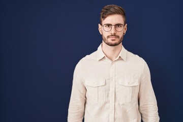 Hispanic man with beard standing over blue background relaxed with serious expression on face. simple and natural looking at the camera.