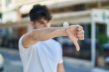Fototapeta na wymiar Young hispanic man doing negative sign with thumb down at street