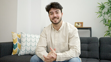 Fototapeta premium Young hispanic man smiling confident sitting on sofa at home