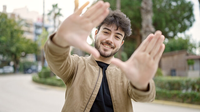 Young hispanic man smiling confident doing frame gesture with hands at park