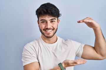 Hispanic man with beard standing over white background gesturing with hands showing big and large...