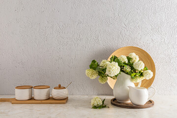 Modern kitchen countertop interior with ceramic jars and a jug with spring flowers against a gray textured wall.