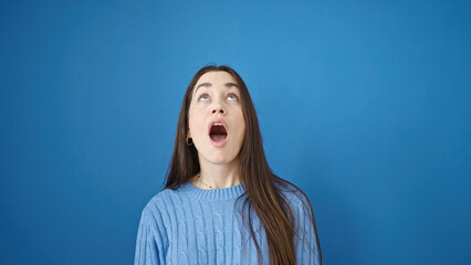 Young caucasian woman standing with surprise expression looking up over isolated blue background