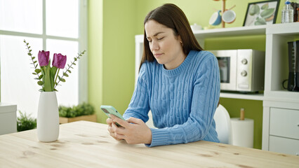 Young caucasian woman using smartphone sitting on table at dinning room
