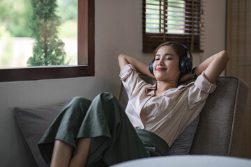 Happy woman relaxing in her sofa at home, Smiling girl is listening to music with headphones and lying down with eyes closed, Enjoy good quality sound, Stress free concept. © wichayada