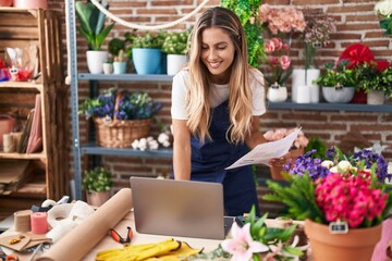 Young blonde woman florist using laptop reading document at florist