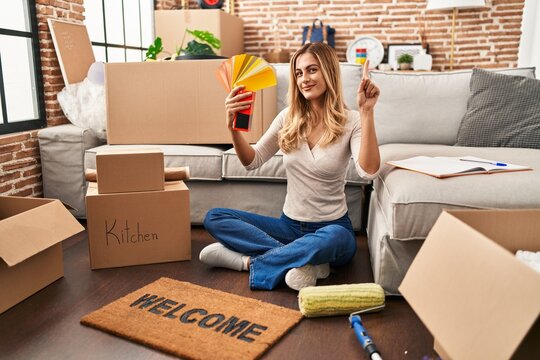 Young blonde woman choosing paint color at new home smiling with an idea or question pointing finger with happy face, number one
