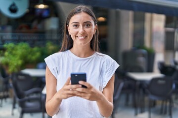 Young beautiful hispanic woman smiling confident using smartphone at coffee shop terrace