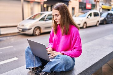 Young woman using laptop sitting on bench at street